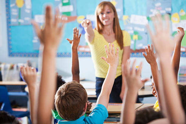 Elementary school class, raising hands Mature woman (40s) teaching class of multi-ethnic elementary school children. Focus on boy in blue shirt. elementary student pointing stock pictures, royalty-free photos & images