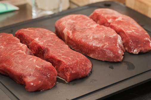 Frozen beef steaks on defrosting plate;