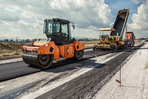 Pavement machine laying fresh asphalt or bitumen on top of the gravel base during highway construction