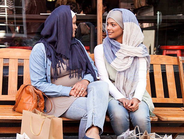 deux femmes musulmanes assis sur le banc après avoir une conversation - muslim cap photos et images de collection