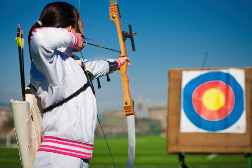 East asian teenage girl archer aiming at target in the playground under blue sky