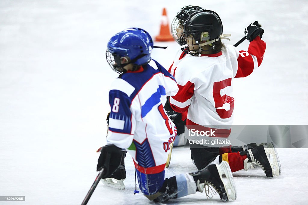 Kids at ice hockey practice. Group of unrecognizable schoolboys during their ice hockey practice.They are kneeling on one knee and waiting for their turn.Wearing red and blue ice hockey jerseys and black helmets. Hockey Stock Photo