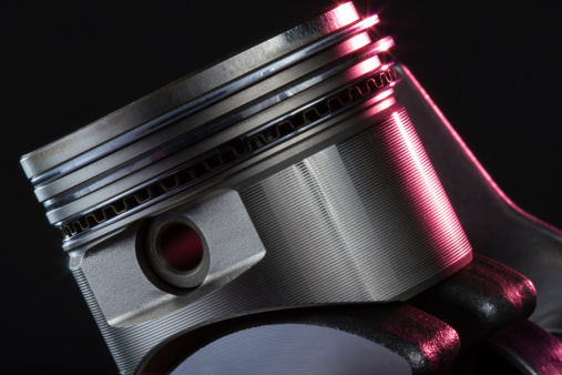 A close up of a single cylinder piston, red highlighted on a black background.