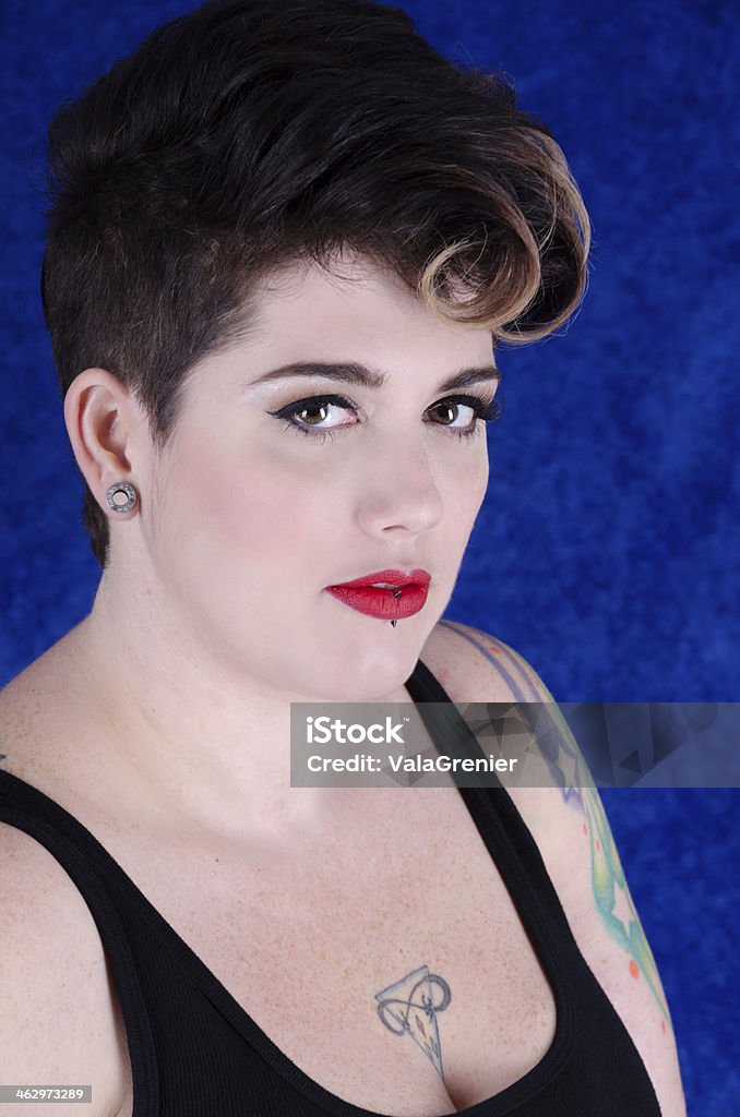 Portrait of 30ish woman with neutral expression. Vertical studio shot on blue crushed velvet of woman with short curly hair and black tank top. 30-34 Years Stock Photo