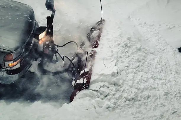 A snowplow operator clears a large snowfall from a parking lot.