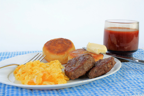 Scrambled eggs with melted cheese and fried sausage patties on plate with buttered biscuits.  Served with small glass of tomato juice on blue gingham place mat for country cooking emphasis.