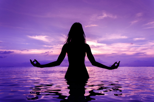 Silhouette of woman sitting in sea and meditating
