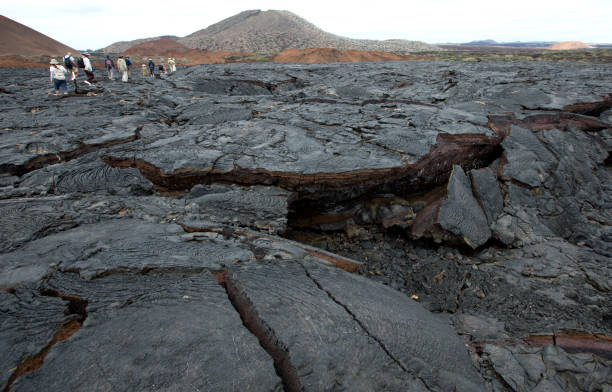 Tourist walking on black lava field Tourist walking on black lava field at Sullivan Bay, Santiago Island in the wondrous Galapagos. isla san salvador stock pictures, royalty-free photos & images