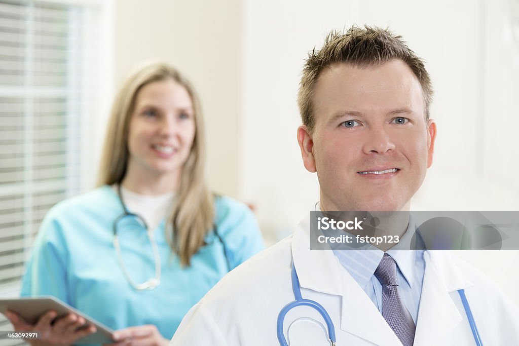 Healthcare: Confident young doctor and nurse in hospital. Kind hospital staff making their rounds to visit patients. Nurse holds digital tablet.  30-39 Years Stock Photo