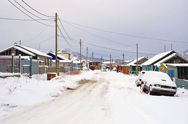 Village winter snow Street village in winter snow. Gray dark gloomy sky. Old wooden house, car, road  in winter covered snow. Township Yuzhno-Kurilsk on the southern Kuril islands, Kunashir island, Russia. kunashir island stock pictures, royalty-free photos & images