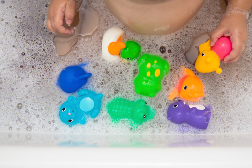 Child in bubble bath playing with bath toys.