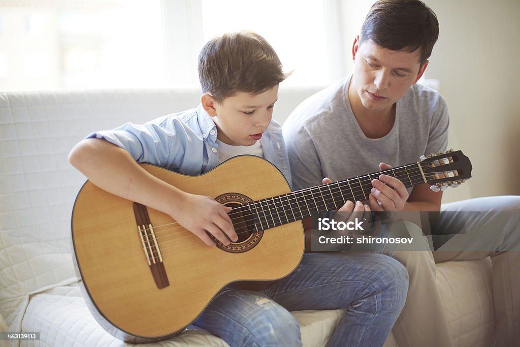 Playing guitar Portrait of handsome young man teaching his son how to play the guitar Acoustic Guitar Stock Photo