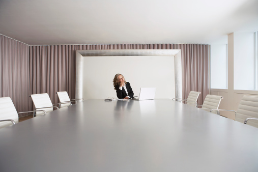 Female business executive sitting alone in boardroom with Laptop
