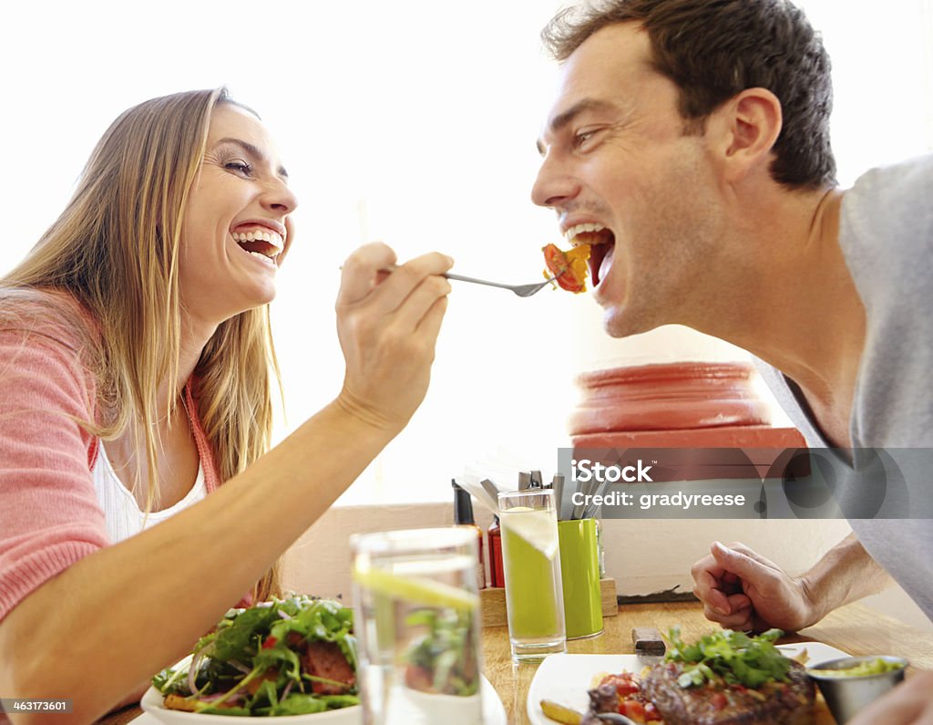 Sharing the taste experience A happy young woman offering her boyfriend a bite of her food in a restaurant Eating Stock Photo