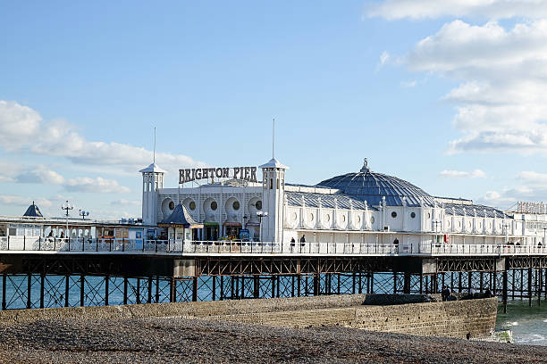 Palace Pier in Brighton, East Sussex, UK Exterior view of the Palace Pier in Brighton, East Sussex, U.K.  The large white building has a sign over the entrance and a large dome in the center.  The blue sky has a few white, fluffy clouds, and the base of the pier is visible under the building. brighton england stock pictures, royalty-free photos & images