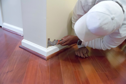 Painter is using a tool on a baseboard in a home, which he is painting.   RM