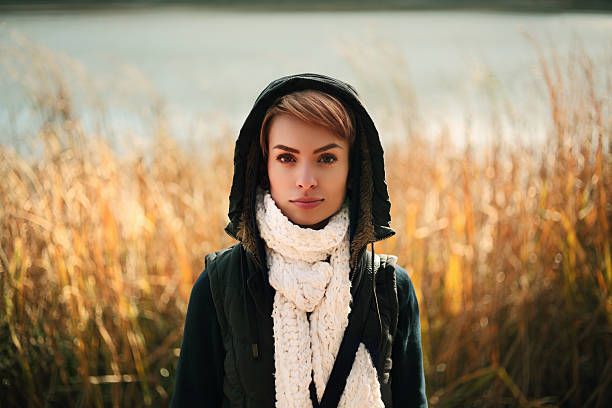 European pretty young woman fashion model in a stylish knitted sweater with a vintage checkered scarf posing outdoors in a field among dry tall grass.Cute girl resting in the countryside in a fall day