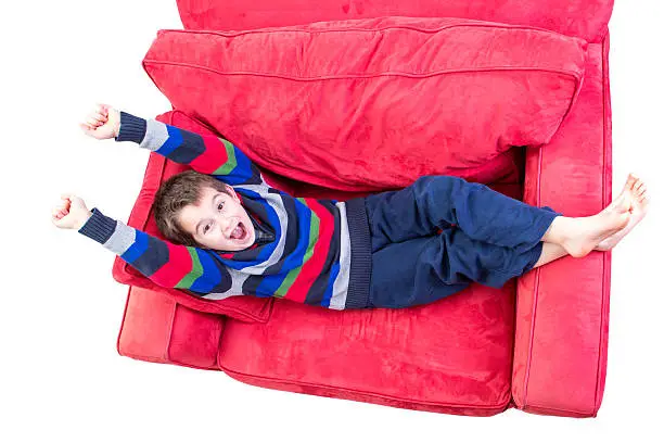 Eight years old kid promoting a feeling of cheer on the red couch, isolated on white