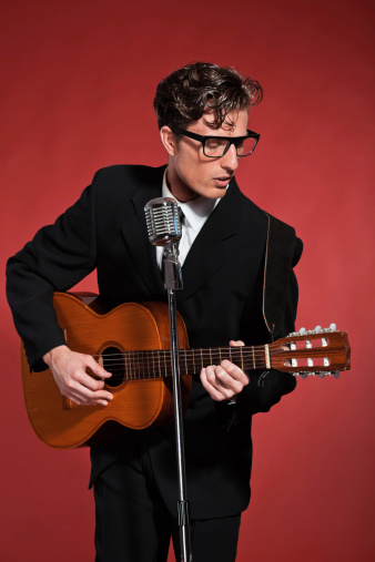 Retro fifties musician with glasses playing acoustic guitar. Studio shot.
