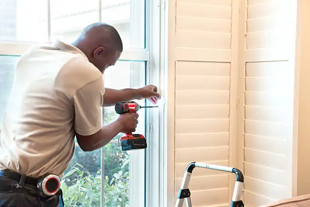 A window treatment installer installs wooden shutters in a residential home.  RM