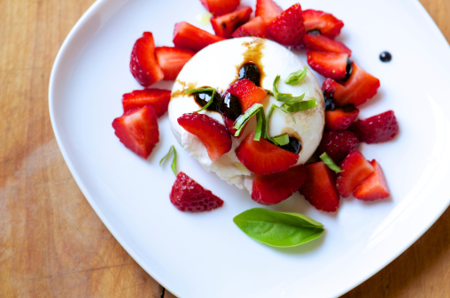 Fresh burrata cheese with strawberries, basil and balsamic syrup on white plate from above