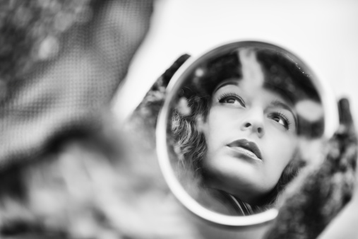 Face's reflection on old mirror of beautiful pensive woman, retro styled image in black and white.