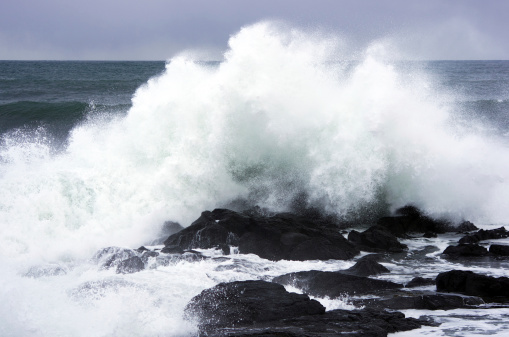 White storm wave crashing on the black rocks, wind breaks sea spray