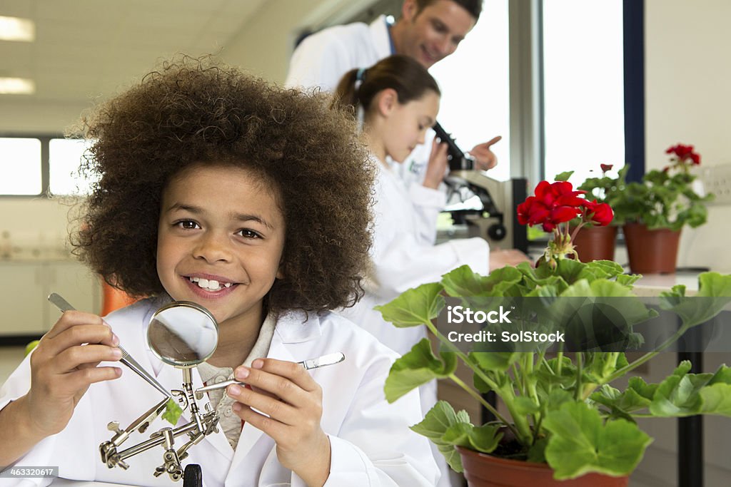 School Science Lab Boy smiles at camera in the foreground and a male adult works with a young girls in the background Child Stock Photo