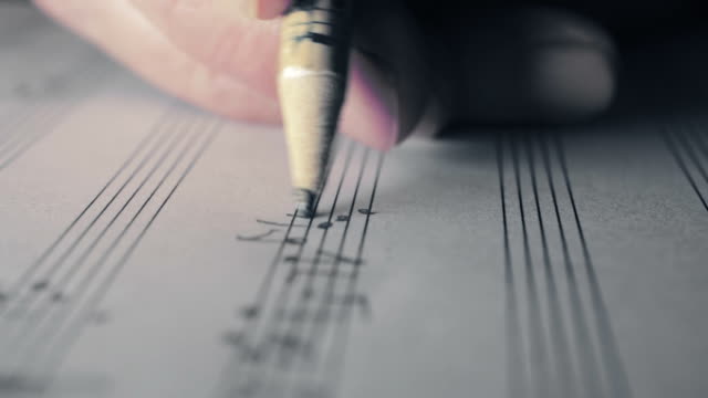 music writing: close up footage of musician composing with a pencil: staff, key