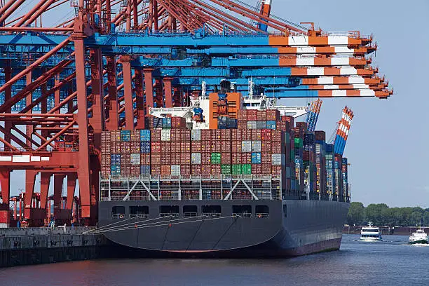 A container gantry crane loads or unloads a container ship with dozens of containers in different colors.