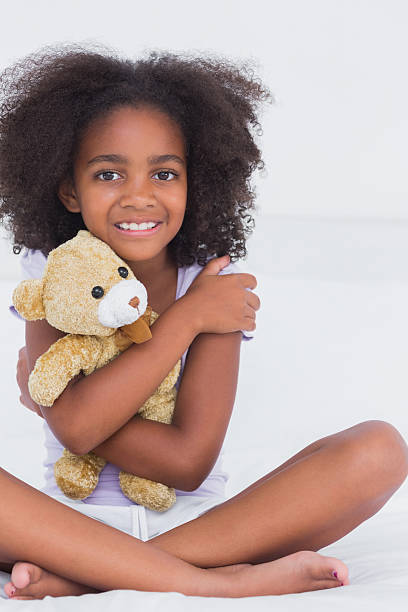 istock Girl sitting on bed smiling at camera holding stuffed bear 463375787