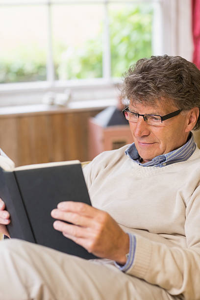 istock Thoughtful mature man reading a book sitting on his sofa 463376343