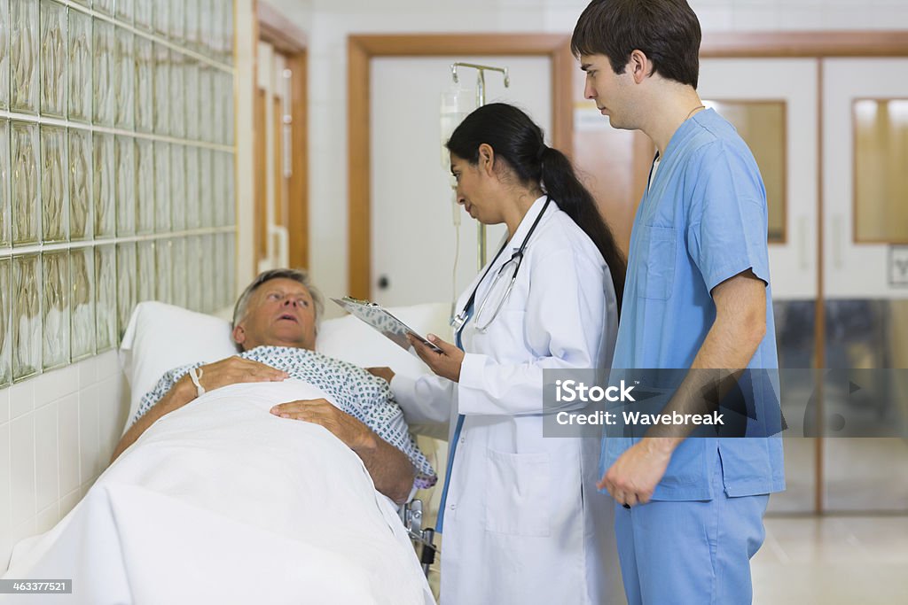 Doctor and nurse examining a patient lying on bed Doctor and nurse examining a patient lying on a bed in a hospital hallway 20-29 Years Stock Photo