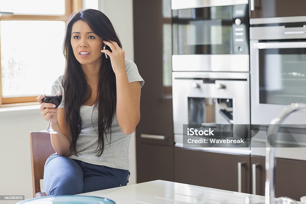 Stressed woman calling in the kitchen Stressed woman calling with glass of wine in the kitchen 20-29 Years Stock Photo