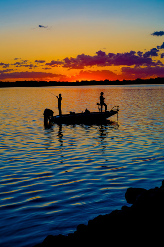 Fisherman in a boat at sunset with vibrant colors.