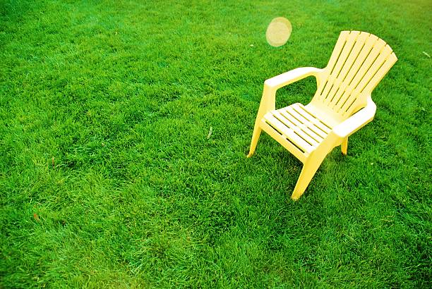 A plastic, yellow lawn chair sitting in green grass.