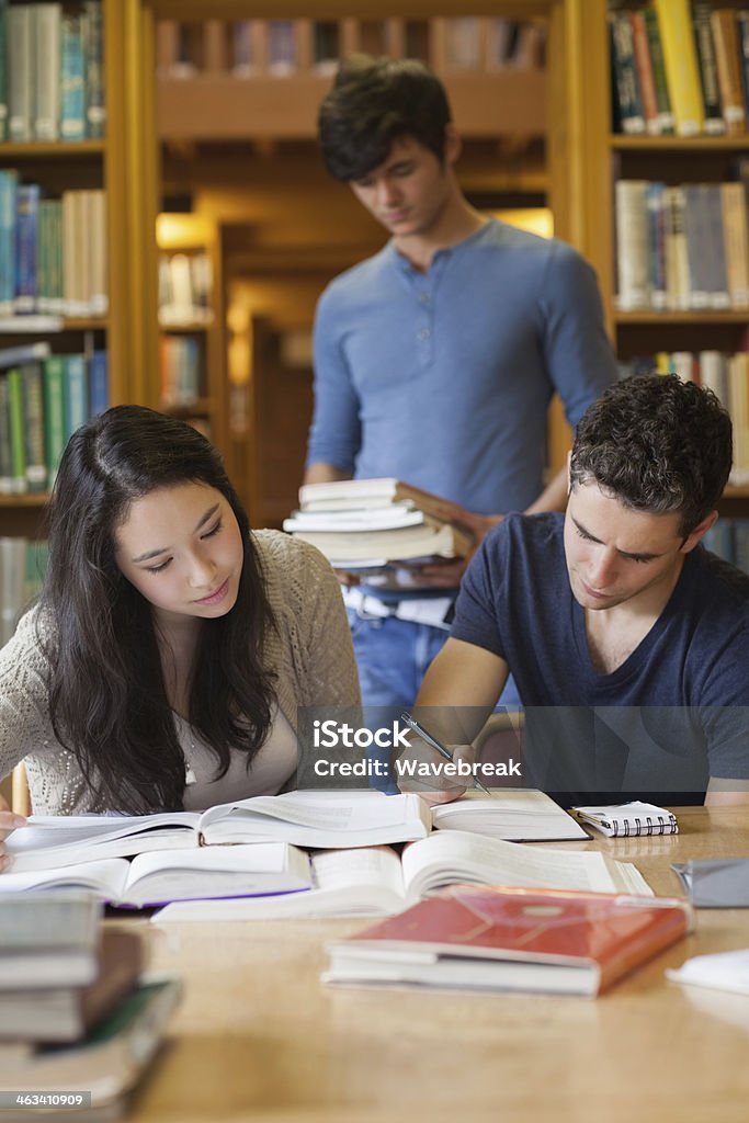 Three people studying in a library Three people in a library studying and looking at stacks of books 20-29 Years Stock Photo