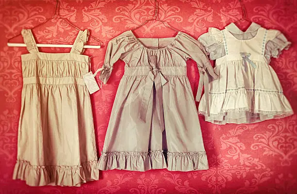 Three little antique child's dresses hanging on hangers.  They are positioned side by side and one has a price tage on it.  Background, texture, grain, and aging added. Copy space.