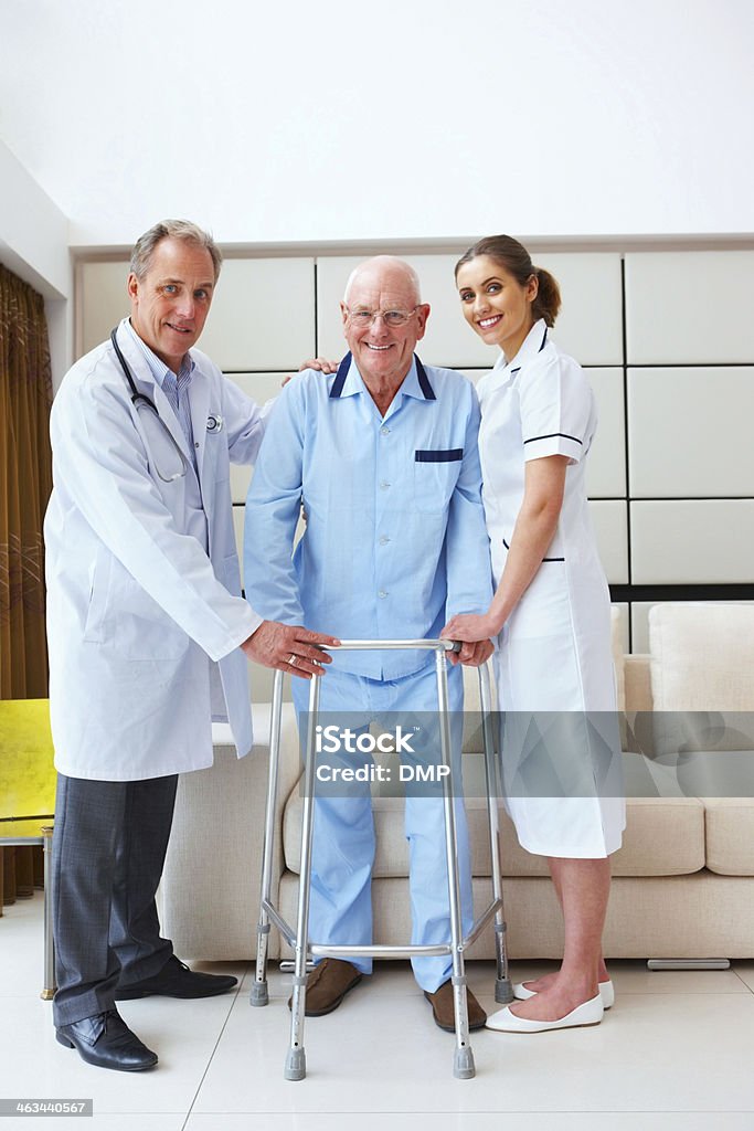 Medical team with disabled senior patient Medical team standing with senior male patient holding a walker in hospital A Helping Hand Stock Photo