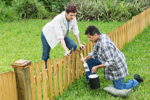 Mature couple (50s, Hispanic / Native American) standing in back yard, painting fence.