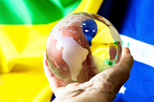 Hand holding crystal world globe showing South America against the Brazilian national flag, symbolizing travel, trade, local culture, and possibly even fortune telling!
