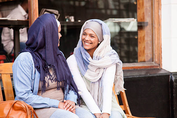 deux femmes musulmanes assis sur le banc après avoir une conversation - muslim cap photos et images de collection