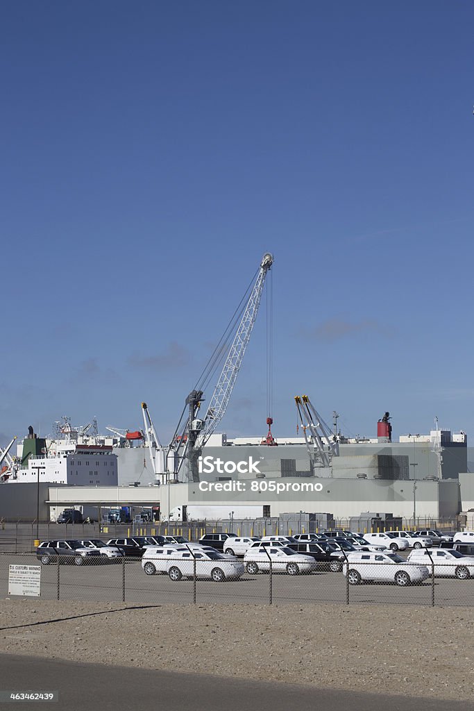 Unloading Cargo from Ship A crane is taking cargo containers off of a cargo ship. In the foreground are many new suv's that have a protective film on them to keep from scrathing the paint while moving. Activity Stock Photo