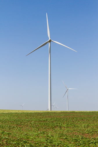 Some eolian turbine on agricultural field against blue sky . Prospective bottom view of a wind turbine in Romania , she gathers wind from the summer breeze and produce energy .