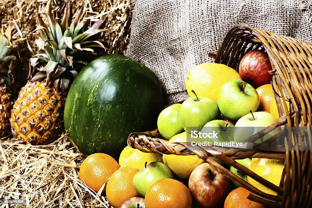 Ripe and ready to eat; fresh fruit at farmers market Fresh, ripe pineapples, watermelon, citrus and apples spilling from a basket onto straw at a farmer's market. Abundance Stock Photo