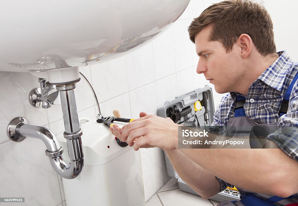 Young plumber fixing a sink in bathroom Portrait of male plumber fixing a sink in bathroom Plumber Stock Photo