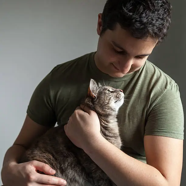 Photo of Caring Man Holding and Looking at Cute Tortoiseshell-Tabby Cat