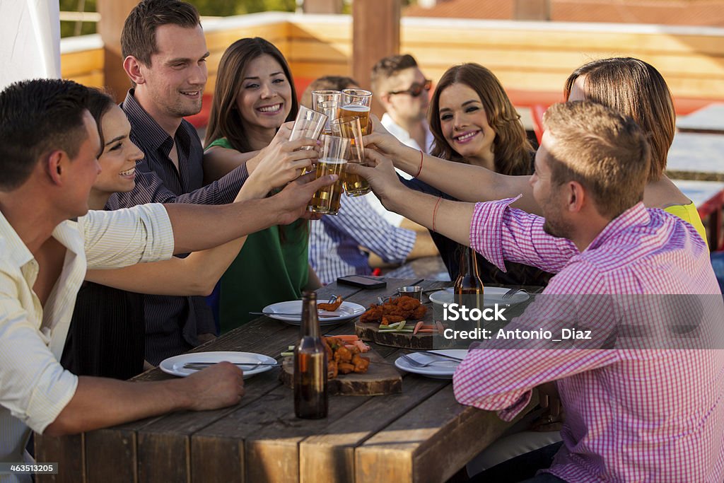 I'll drink to that! Large group of friends having fun and drinking beer at a restaurant Patio Stock Photo