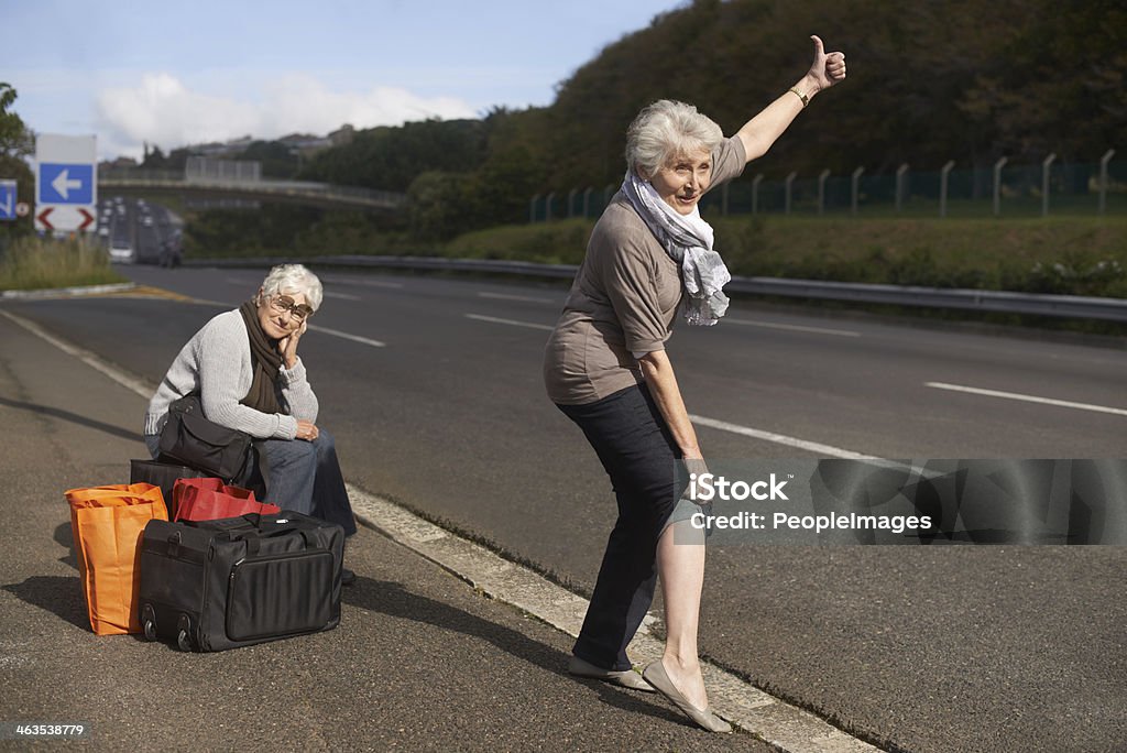 Making their escape from the retirement village... Two senior ladies hitch-hiking by the side of the road Human Leg Stock Photo
