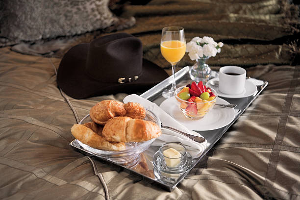 Room Service Tray on bed Room service tray with croissants, fruit and orange juice sitting on hotel bed with cowboy hat. silver platter stock pictures, royalty-free photos & images